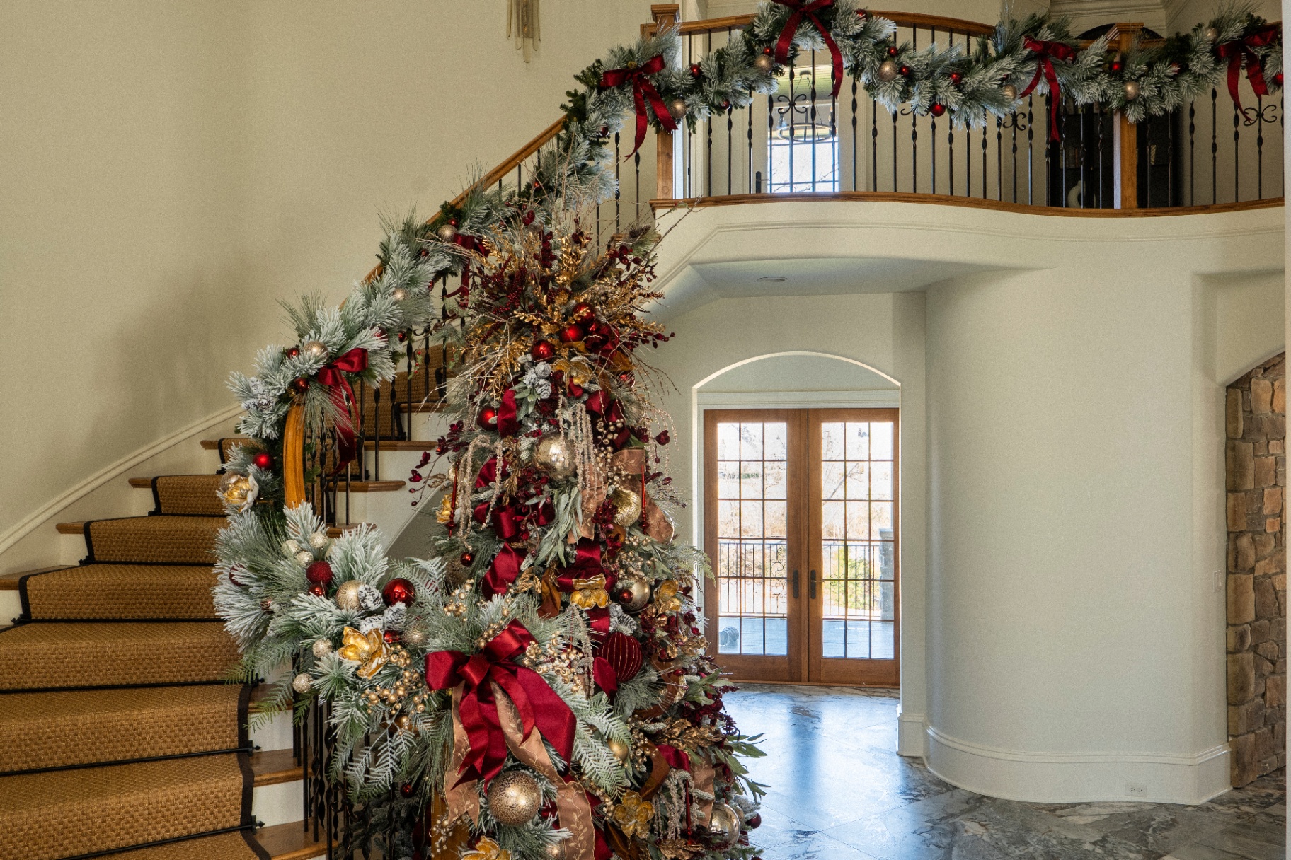 Flocked garland with burgundy bows on a curved staircase and balcony