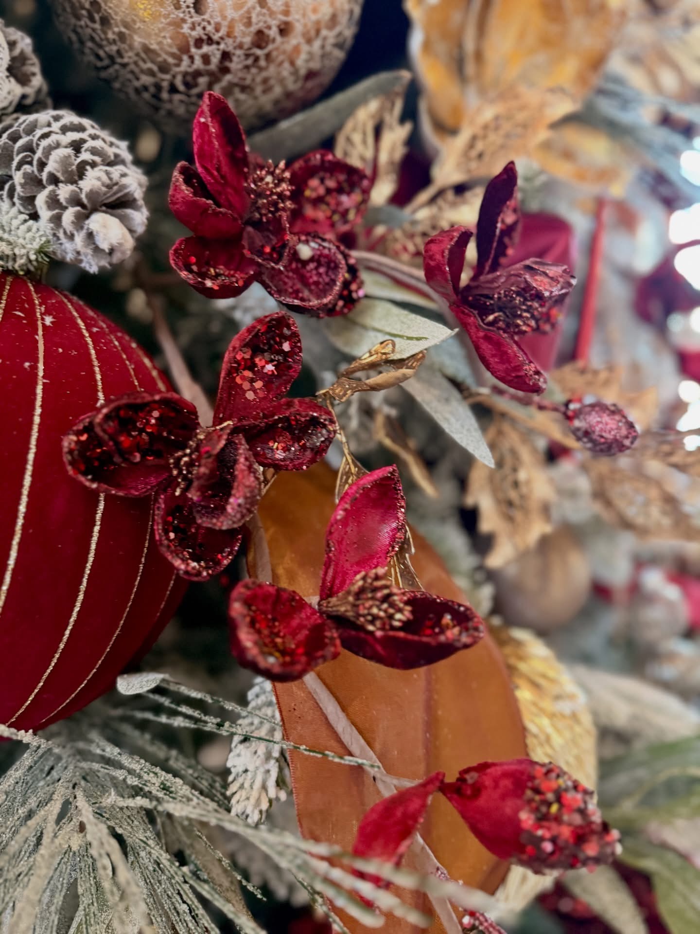 Close-up of deep burgundy glittered velvet blooms with copper ribbon and frosted greenery on a Christmas tree
