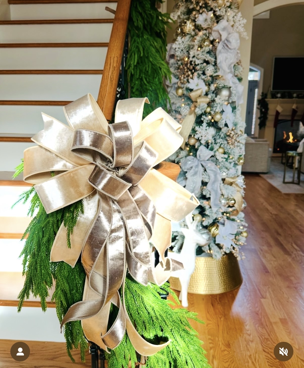 Lush champagne velvet bow on a staircase banister with fresh Norfolk pine garland and a flocked tree in the background