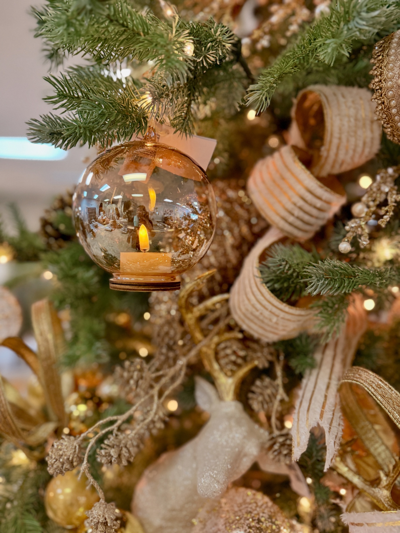 Close-up of a gold mercury glass globe ornament on a tree with burlap ribbon curls and gold pinecone picks