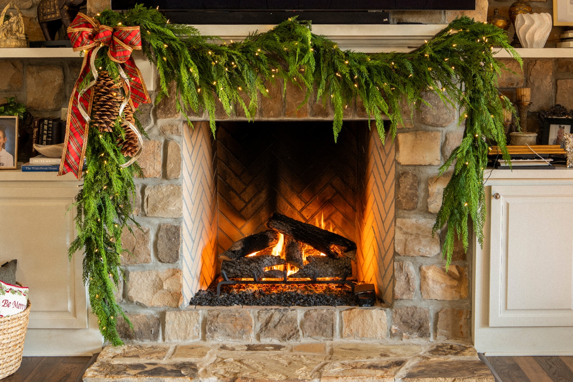 Stone fireplace with lush cedar garland, white lights, and a tartan ribbon with pinecones