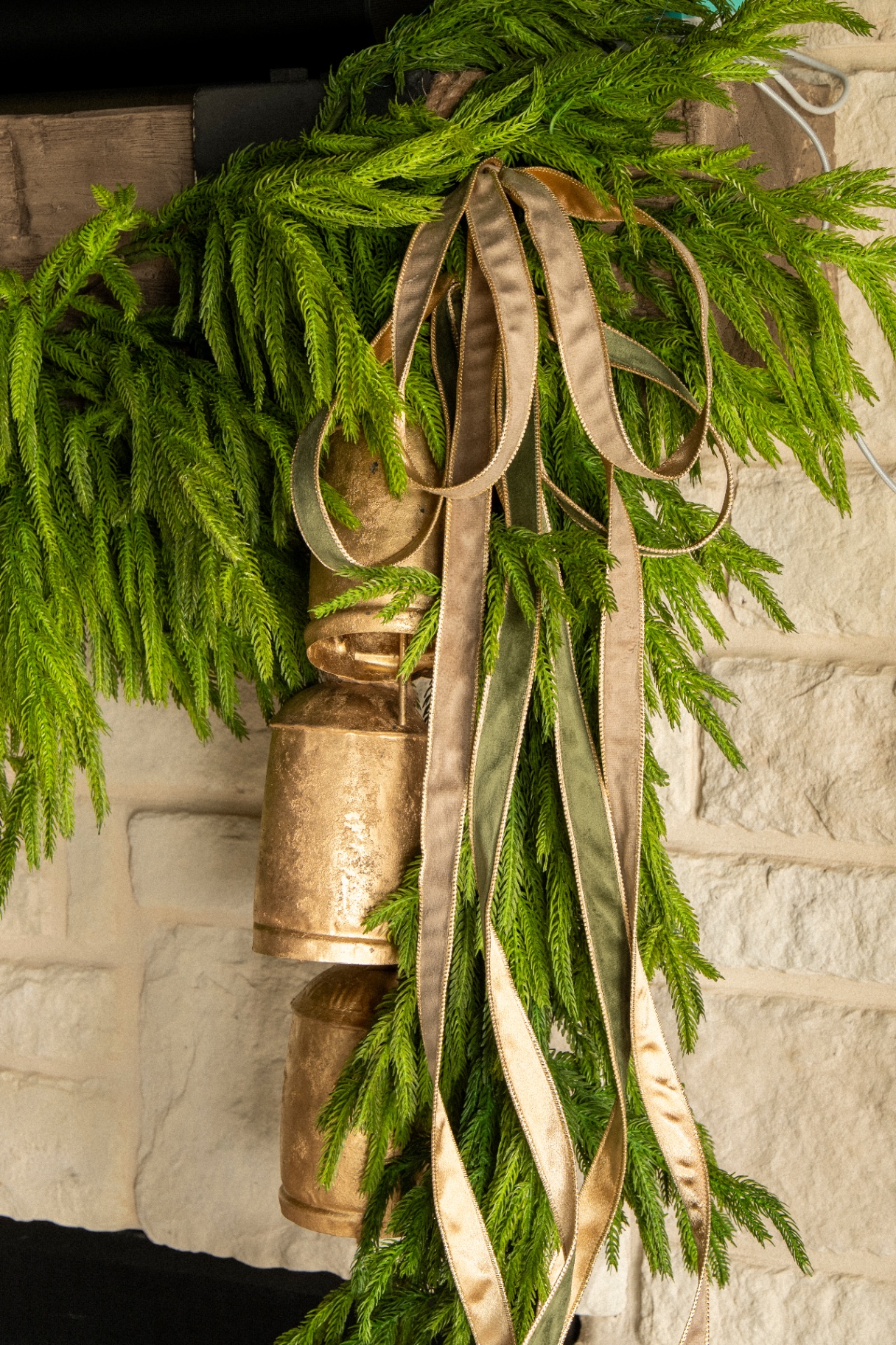 Close-up of antique brass bells nestled in Norfolk pine garland with gold and olive velvet ribbons