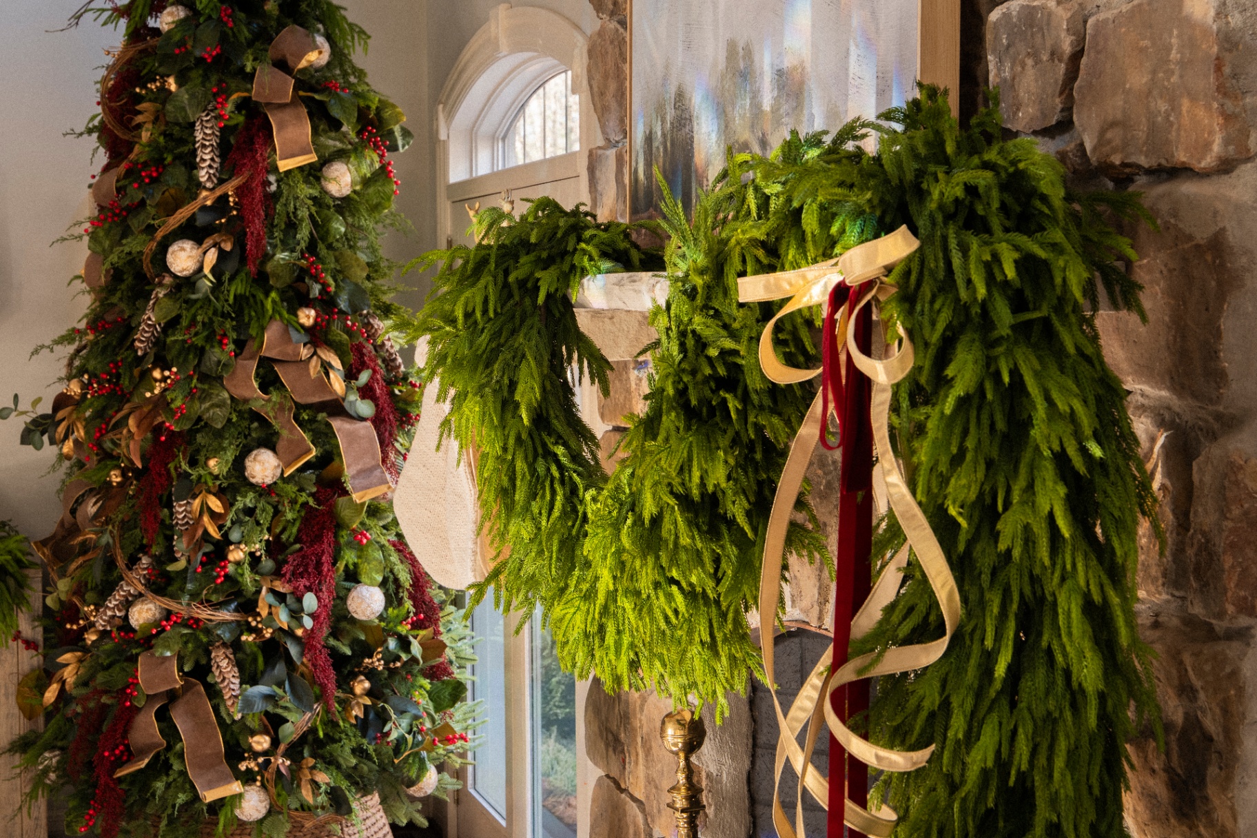 Fresh cedar mantle swags with gold and burgundy ribbon beside a decorated tree