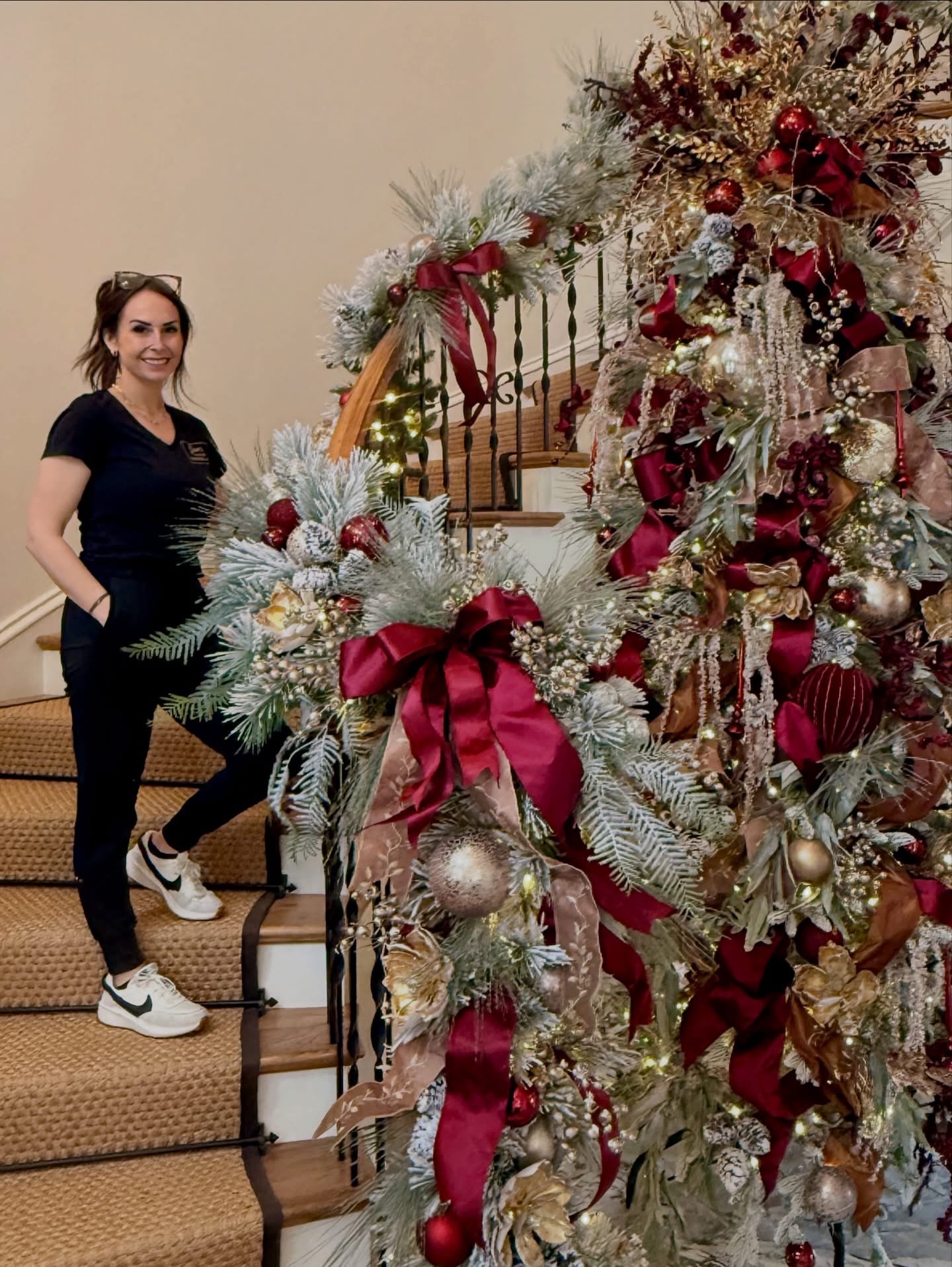 Jen standing on the staircase next to a grand burgundy and gold Christmas tree with flocked garland