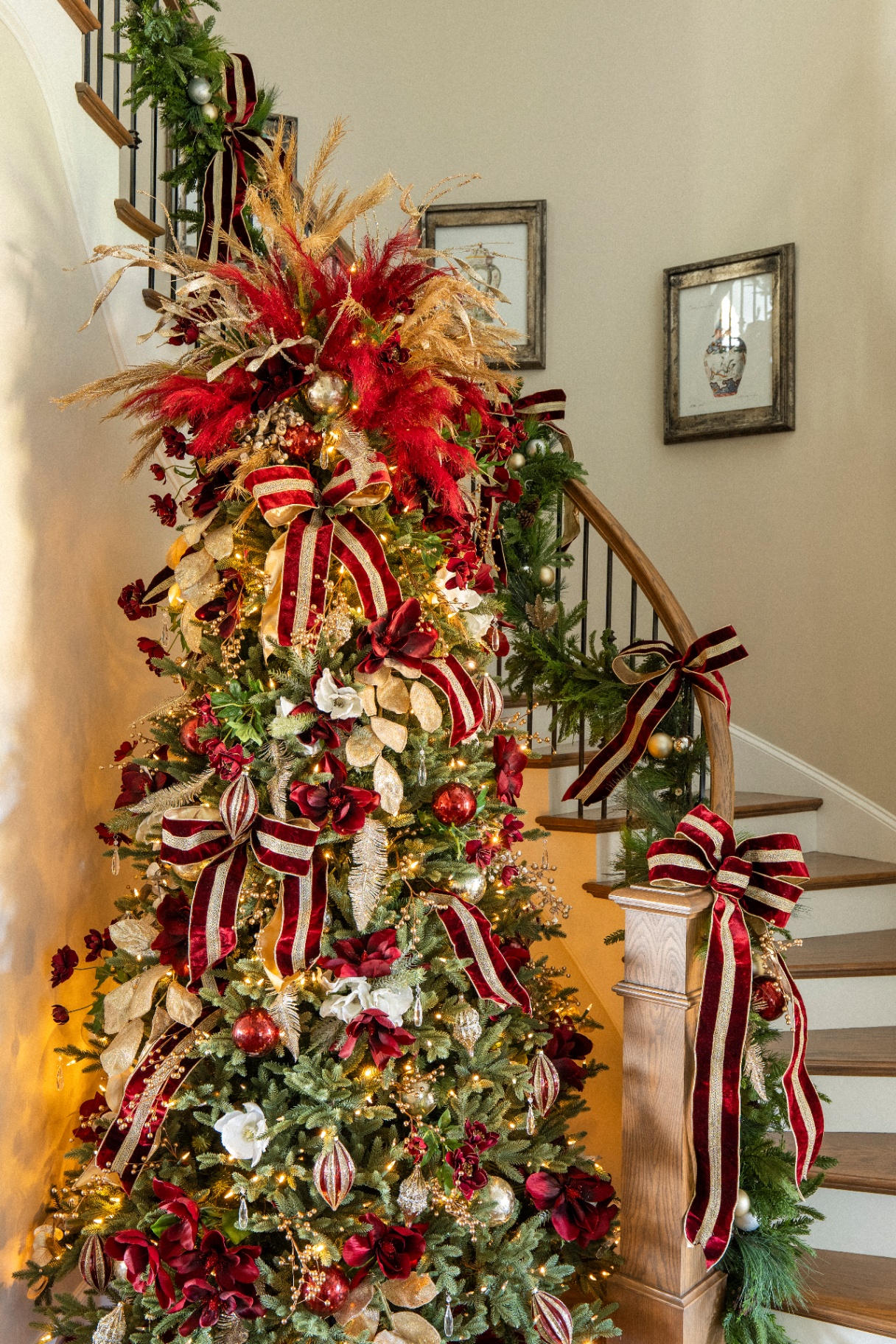 Towering burgundy and gold Christmas tree at the foot of a curved staircase